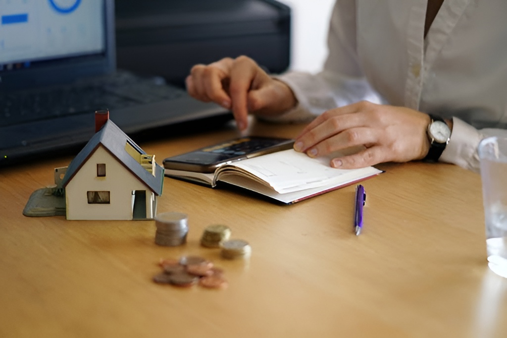 A person calculating with a phone and a miniature house with coins.